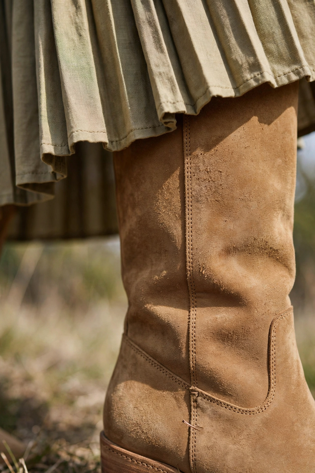 Close-up of tan suede knee-high boots with a pleated midi skirt