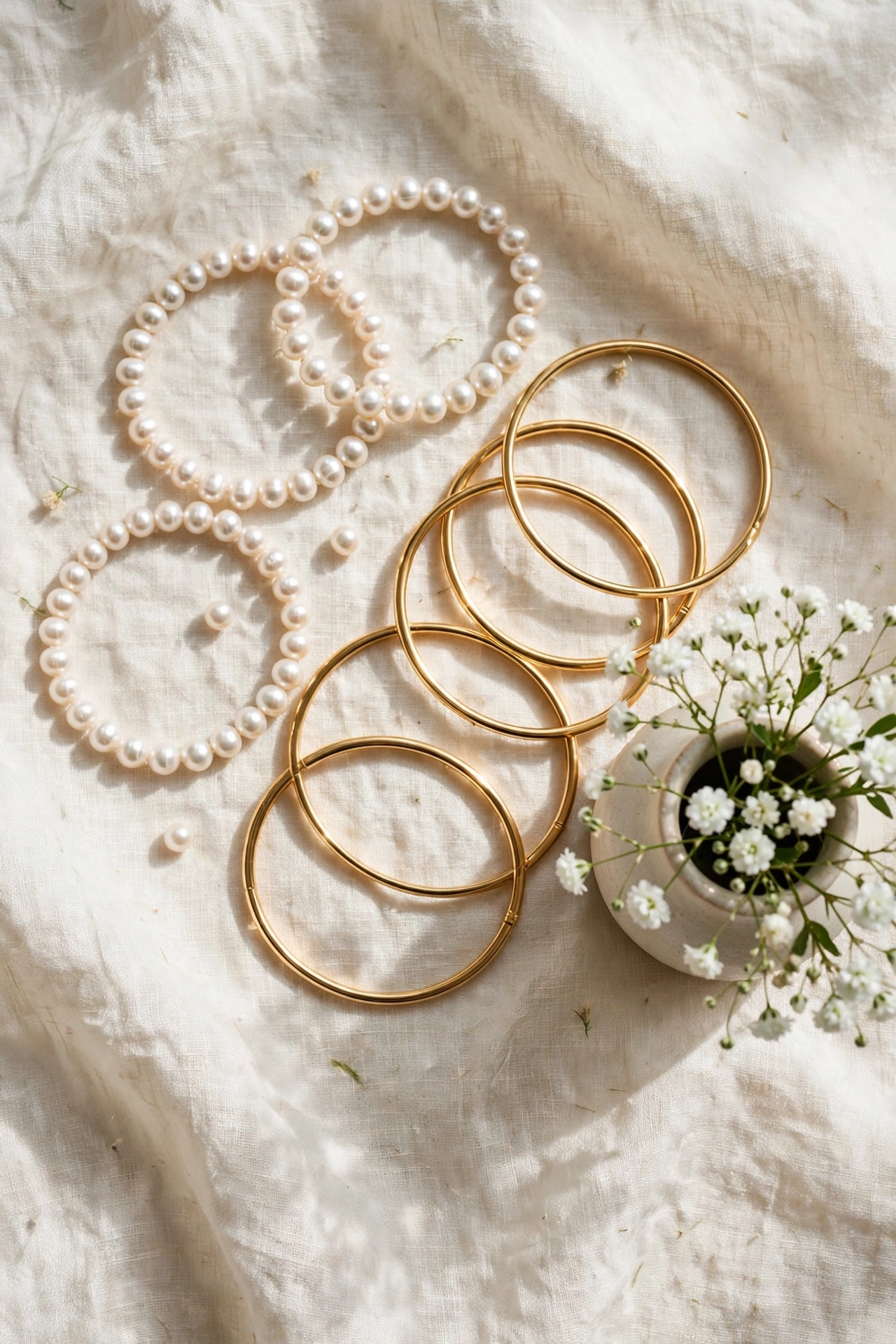 Flat lay of pearl bracelets and gold bangles arranged on cream linen