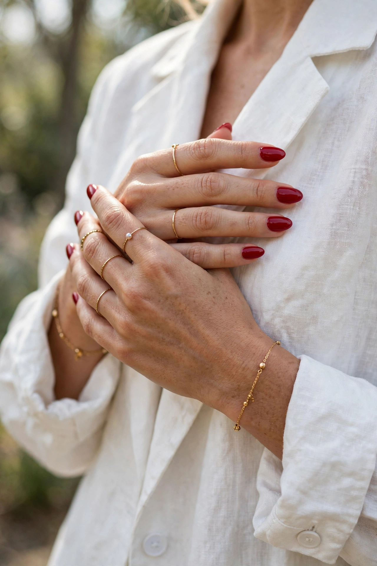 Red manicured hands paired with a white outfit and delicate gold jewellery