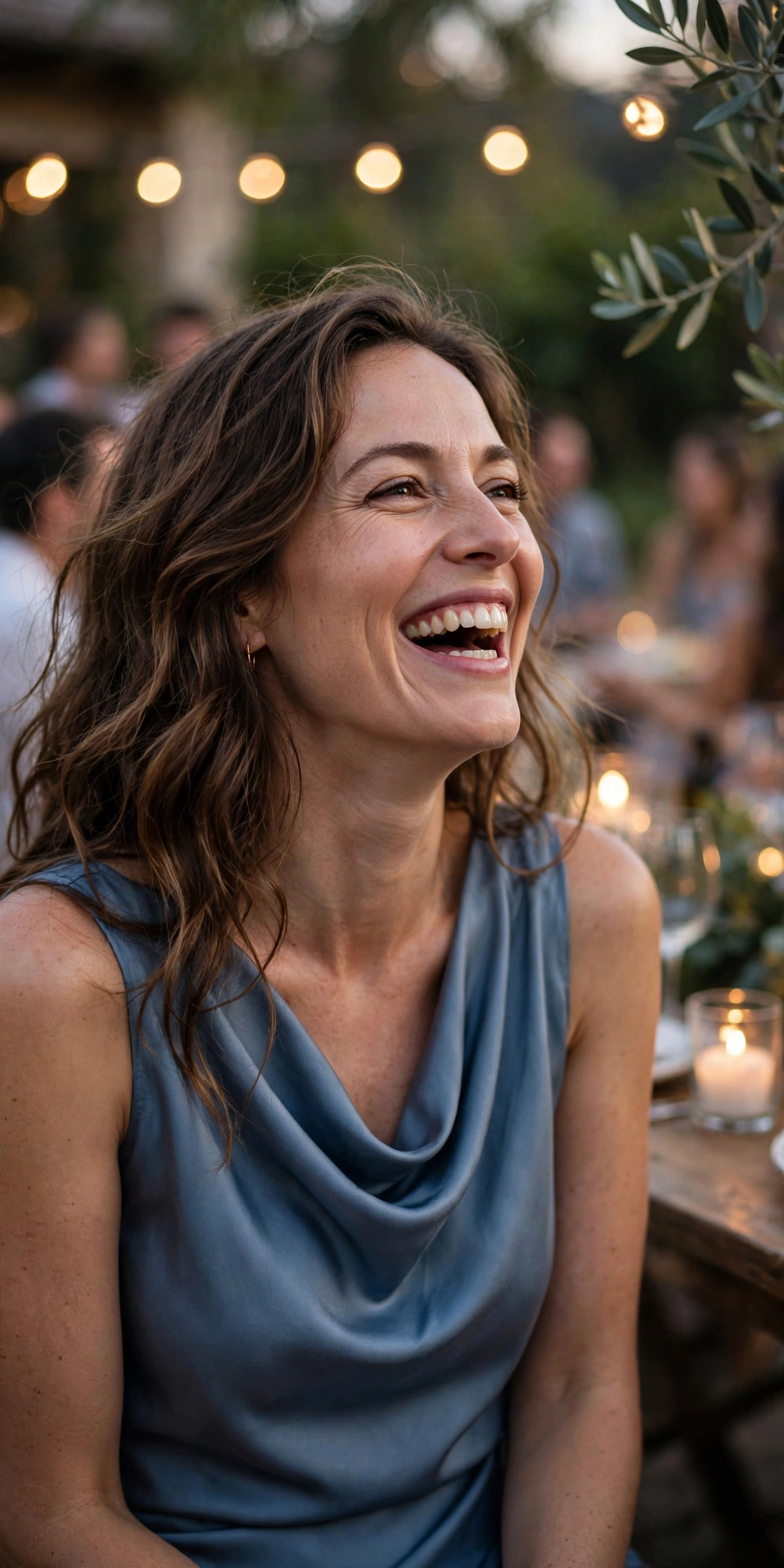 Woman in a dusty blue satin cowl dress laughing at an outdoor evening gathering